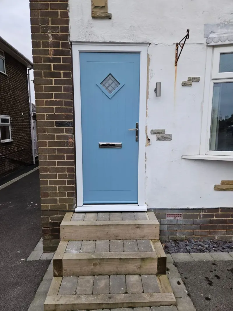 Powder-blue cottage door with diamond-patterned glass, set in white render above sleeper steps.