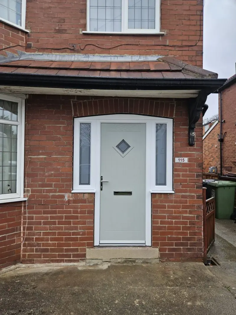 Sage-green cottage door with diamond glazing and white sidelights, set in an arched brick porch, house number 115.